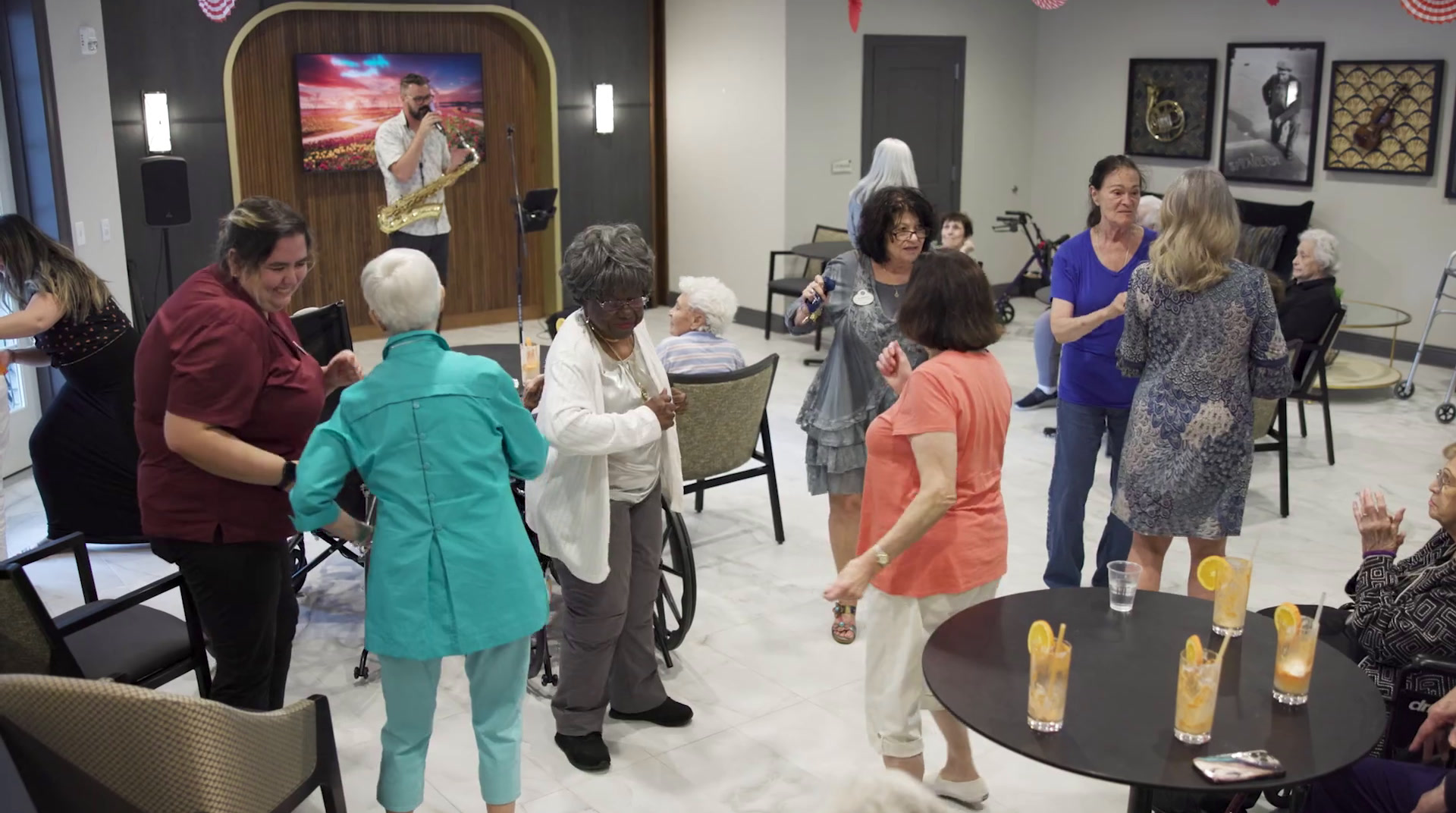 Community members dance and mingle as a performer entertains from a small stage, with orange-garnished drinks set on a nearby table, during a lively social gathering at Arbor Terrace Highland Park that celebrates an active senior lifestyle Highland Park IL and senior living Highland Park IL.