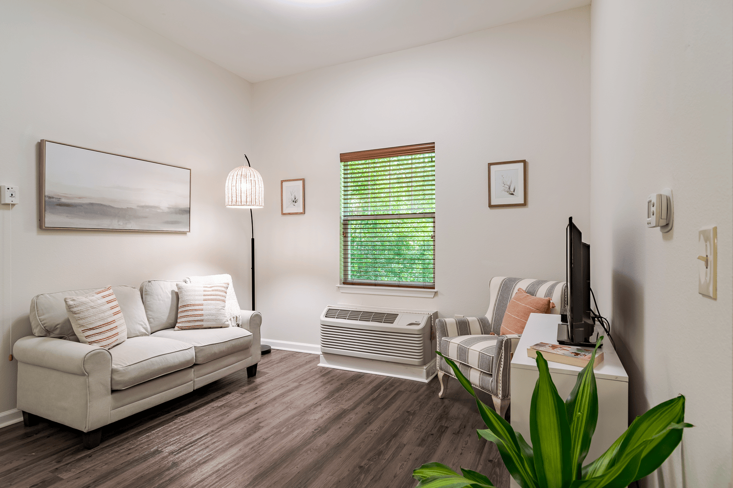 Cozy model living area with plush seating, a leafy plant, and large windows, showcasing the comfortable layout of senior apartments in Alpharetta, GA and independent living in Alpharetta, GA.
