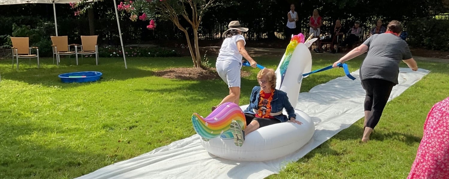 Senior lady riding a unicorn floatie on a slipnslide