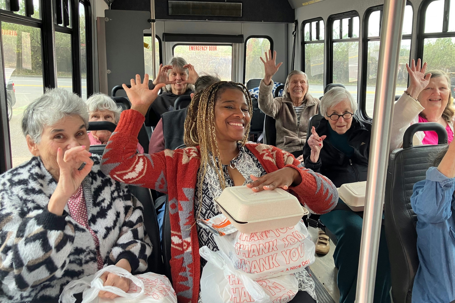 A group of senior residents out on a road trip with a staff member whole they enjoy meals during the drive