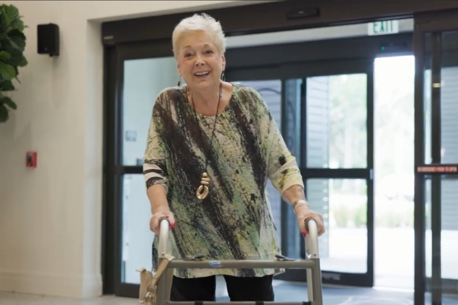 A smiling woman walks with a walker through a bright, modern hallway at The Arbor at Delray, reflecting the supportive, wellness-focused environment of senior living in Delray Beach, FL.