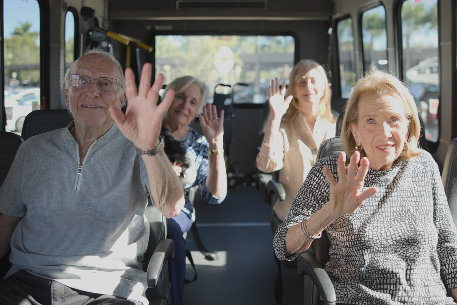 Residents wave cheerfully from a community shuttle before heading out on an outing, reflecting the active, engaging senior living lifestyle enjoyed throughout this senior living community.