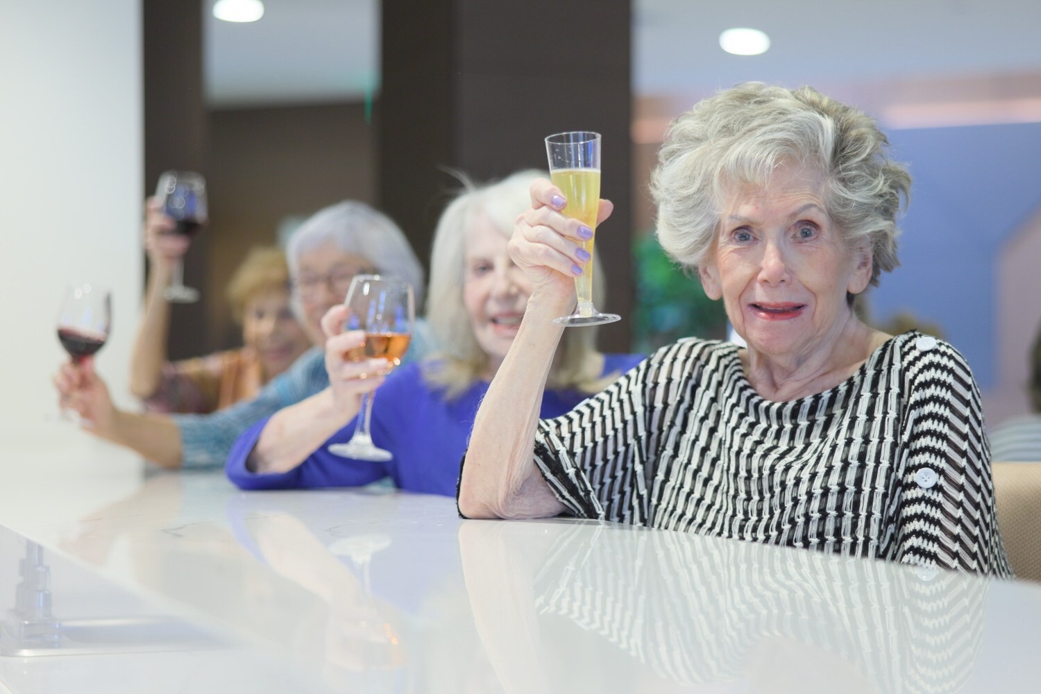 Residents raise their glasses in a toast together at the bar during a social gathering at The Arbor at Delray, reflecting the vibrant social calendar in this Delray Beach, FL senior living community.