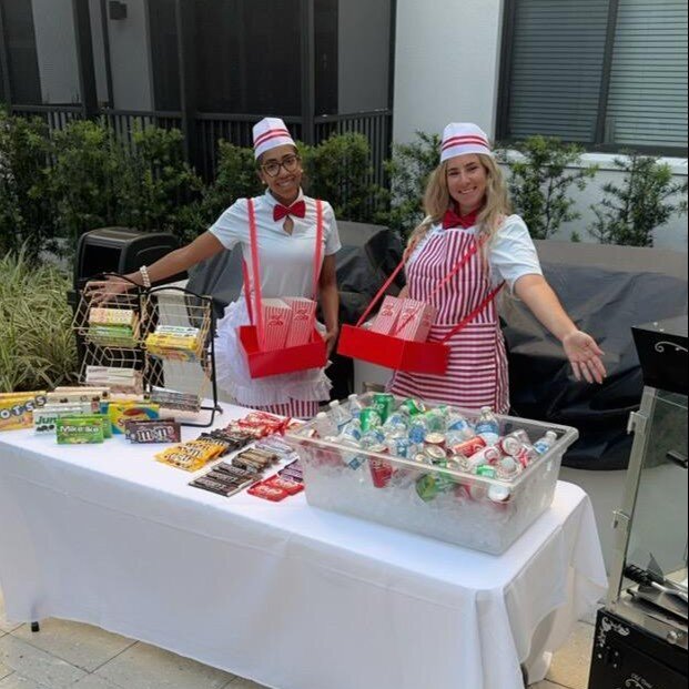 Two staff members smile behind a festively decorated outdoor food station at The Arbor at Delray, showcasing the warm social engagement and community spirit of senior living in Delray Beach, FL.