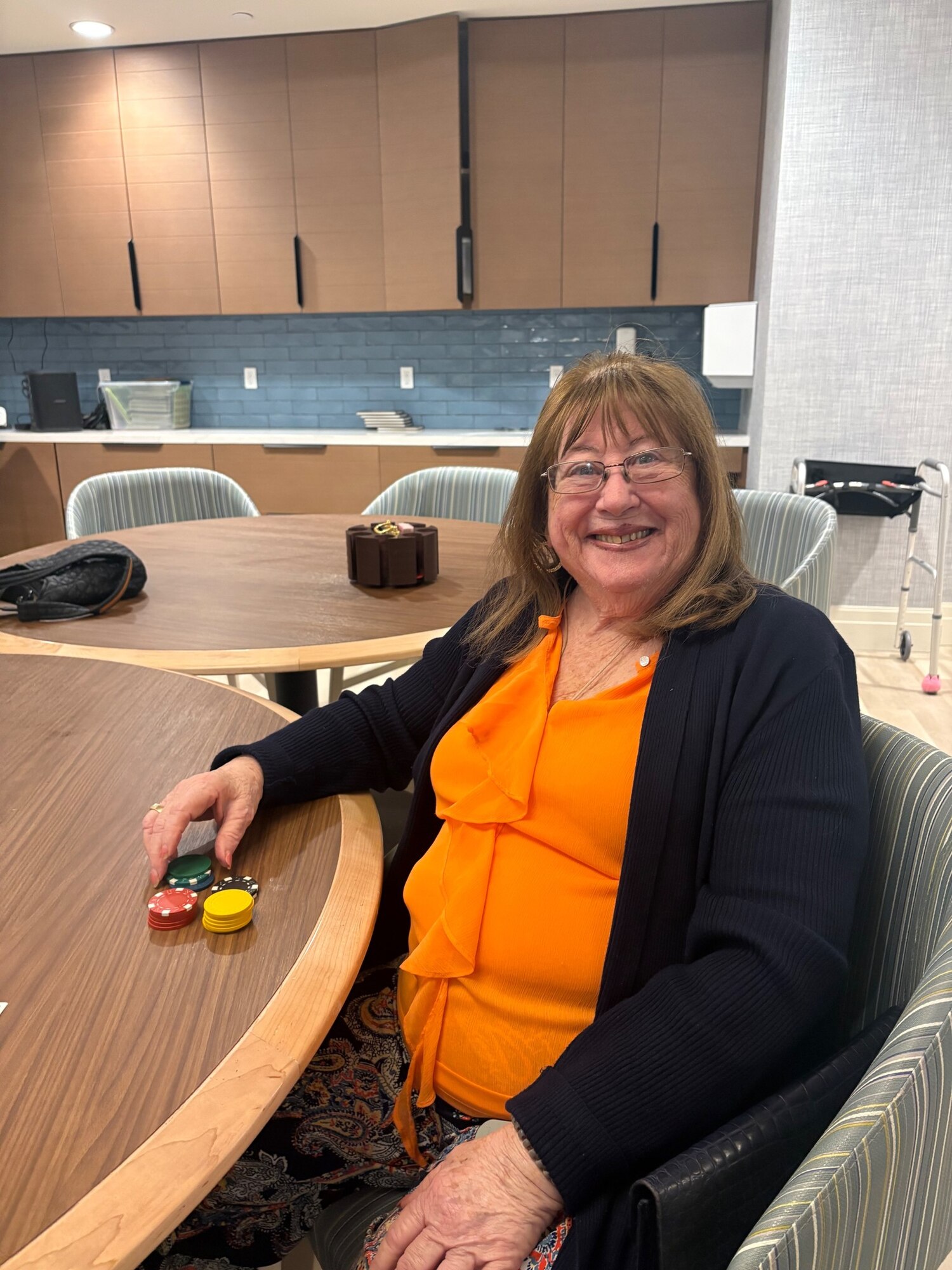 A smiling woman enjoys a game of poker chips at a round table in a stylish common room, highlighting the fun, engaging lifestyle offered at this active senior living community in Delray Beach, FL.