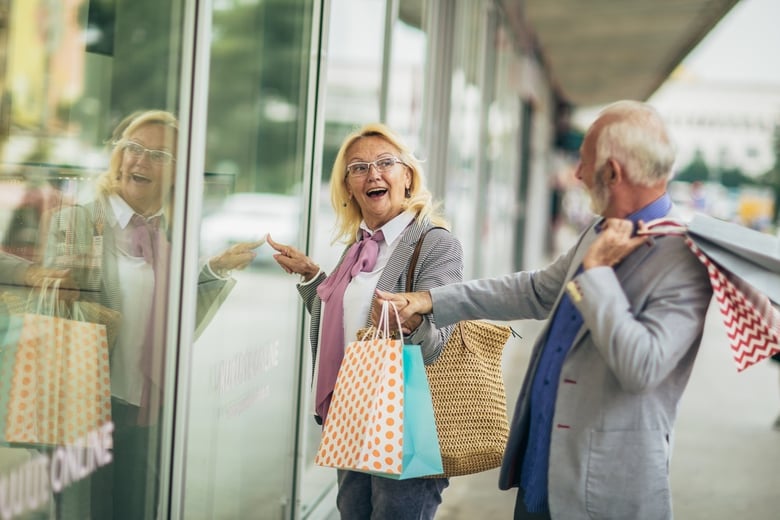 Two people smile and chat while holding shopping bags near a storefront, reflecting the everyday conveniences available to residents at senior living near Jamison, PA, close to Warrington.