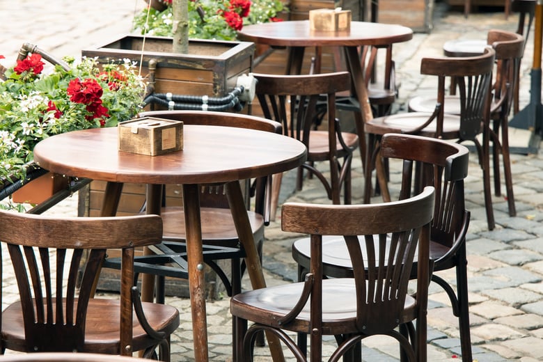A cozy outdoor café patio with round tables, wooden chairs, and blooming red flowers, near senior living near Southampton, PA — convenient assisted living close to Warrington.