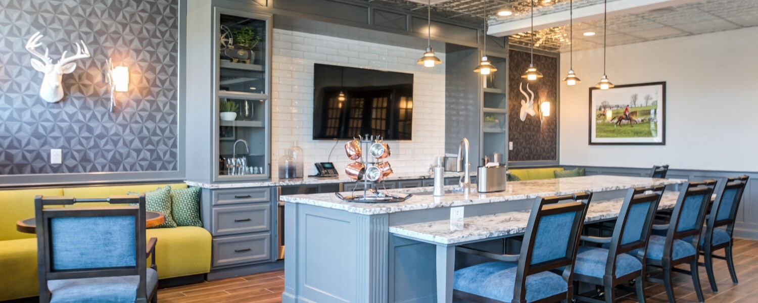 Community lounge and kitchen space in Exton, PA with a stone-top island, cozy blue seating, and warm pendant lighting, part of the resort-style senior living Exton, PA residents enjoy daily.