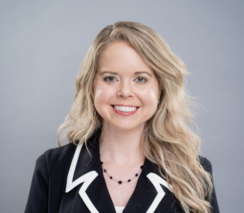Megan Wardlaw, Community Sales Director, smiles in a black and white blazer and beaded necklace against a soft gray backdrop, welcoming families to senior living in Malvern, PA, and assisted living communities in Exton, PA.