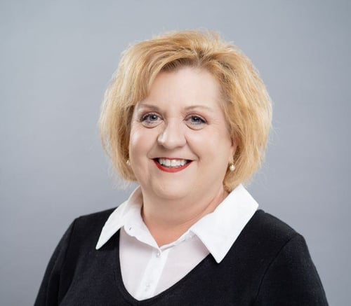 Sue Haines, Executive Director, smiles warmly in a white collared shirt and black sweater against a soft gray backdrop, leading the team at senior living in Exton, PA, and assisted living in Exton, PA.