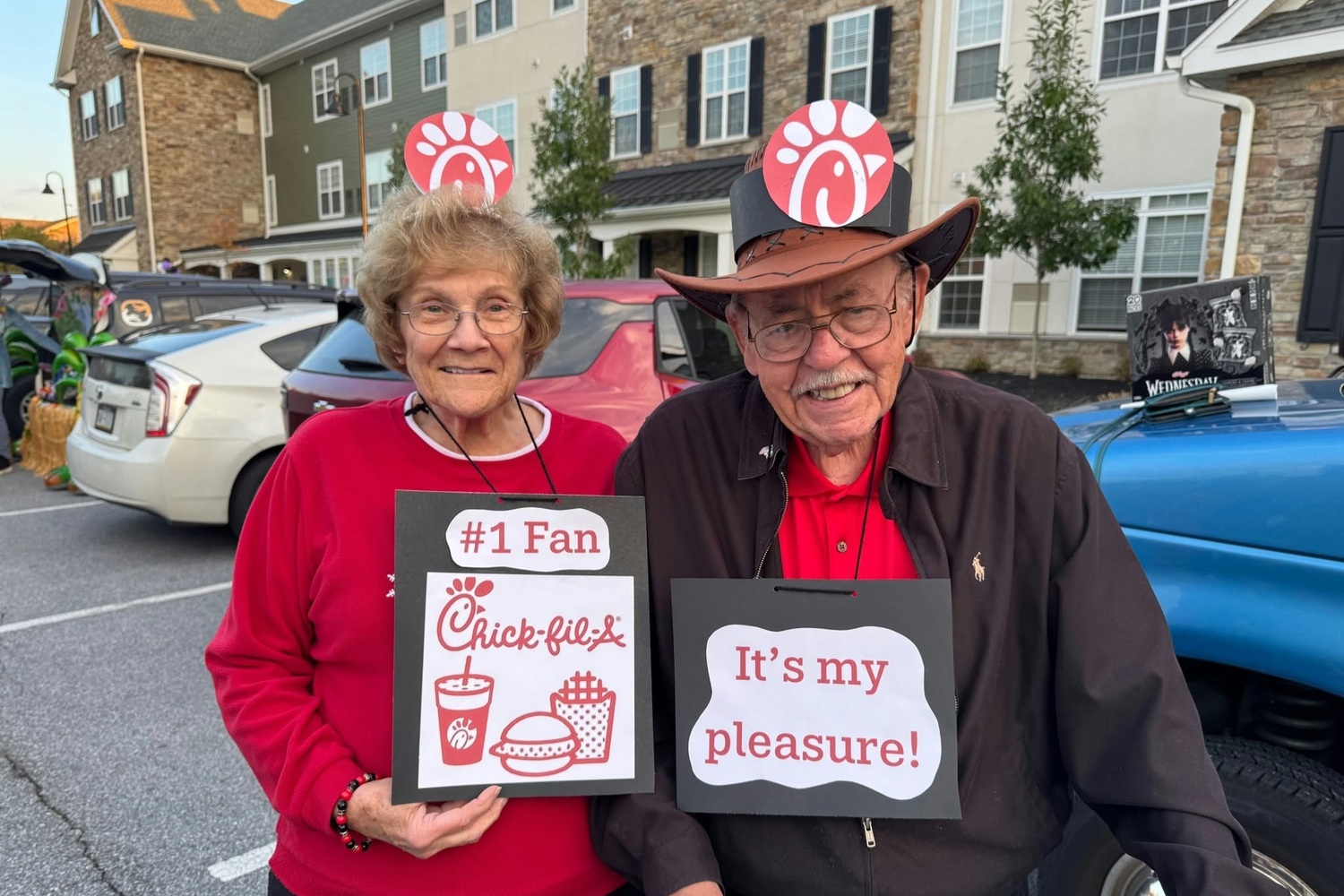 Two residents wearing festive headbands hold handmade signs celebrating a favorite restaurant during a sunny outdoor Halloween gathering, reflecting the community spirit of senior living in Downingtown, PA and senior living near West Chester, PA.