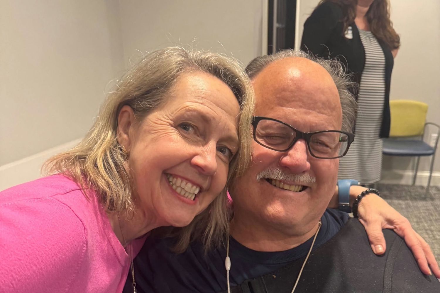 Two residents share a warm embrace and big smiles in a bright community space, capturing the friendly connections found through senior living near me Exton, PA and senior living in King of Prussia, PA.