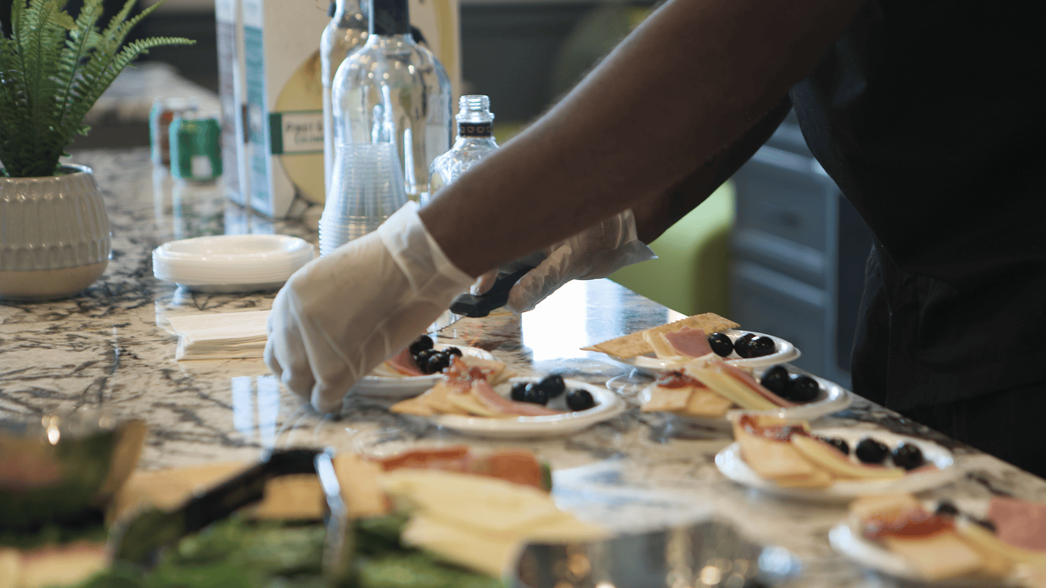 A staff member carefully arranges charcuterie plates with cheese, meats, and olives on an elegant marble counter at Arbor Terrace Waugh Chapel, showcasing the thoughtful culinary presentation and resort-style dining experience at this senior living community in Gambrills, MD.