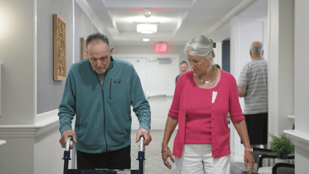 Resident male with a walker and female in a pink sweater walking down the hallway