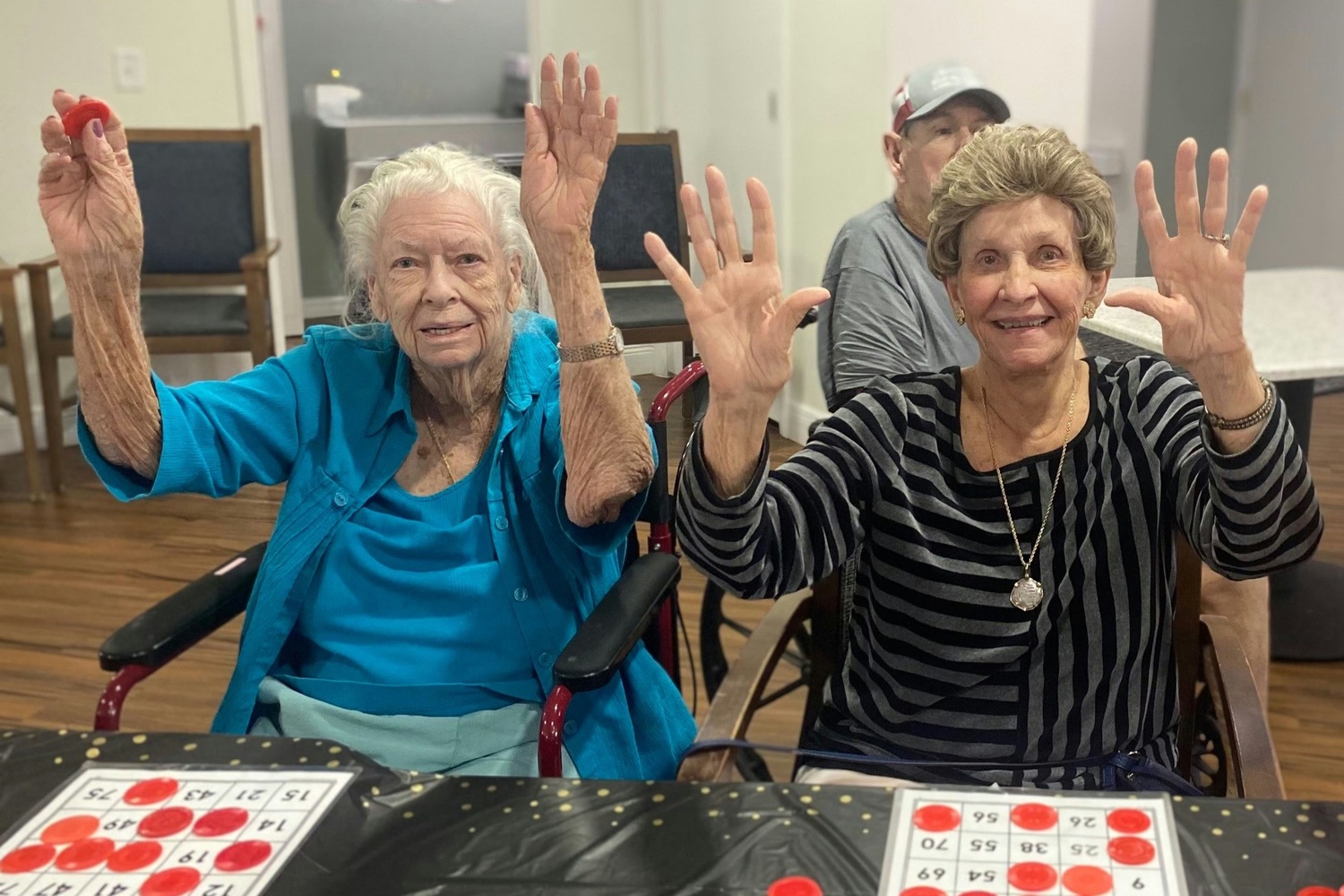 Two residents wave their hands joyfully while playing bingo at Barrington Terrace assisted living in Fort Myers, FL.