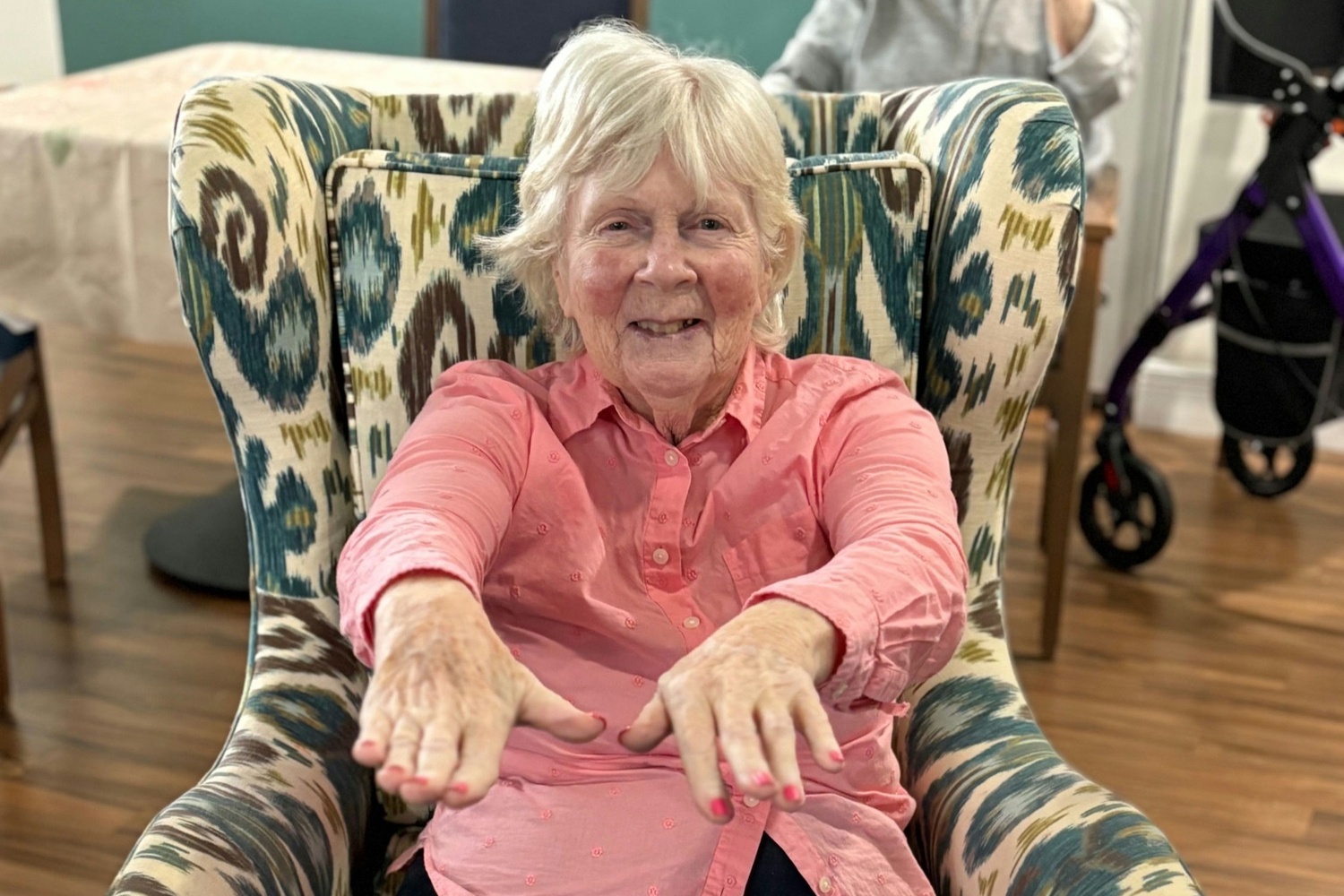 A resident smiles brightly while seated in a patterned armchair during an exercise or wellness activity at Barrington Terrace senior living in Fort Myers, FL.