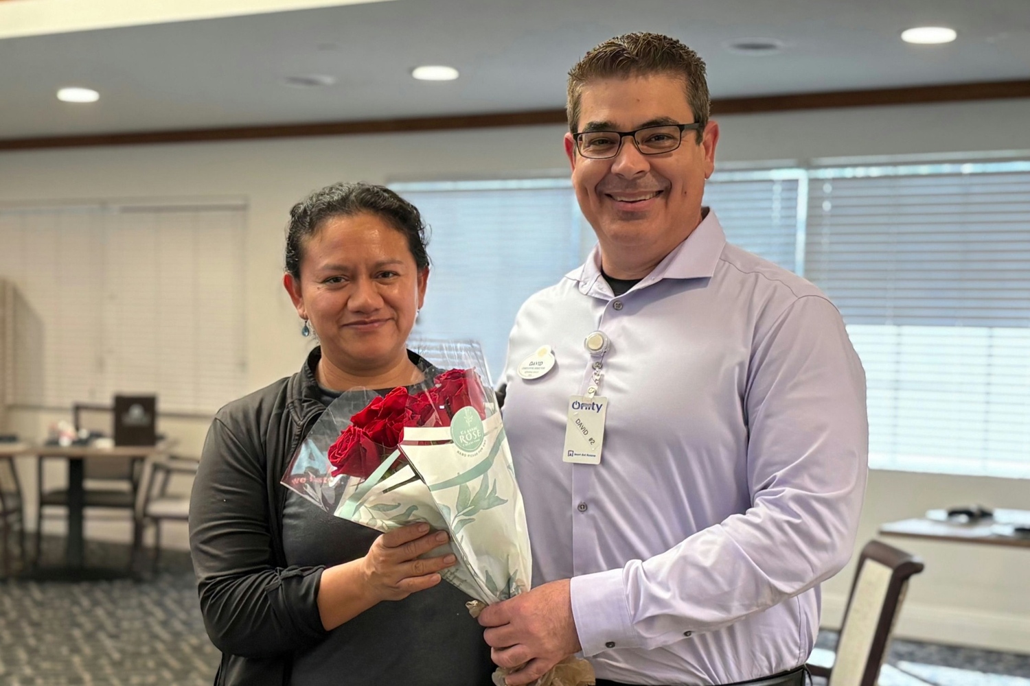 A staff member is presented with a bouquet of red roses by a colleague at Barrington Terrace, an assisted living community in Fort Myers, FL, reflecting the appreciation and team spirit that make this community special.