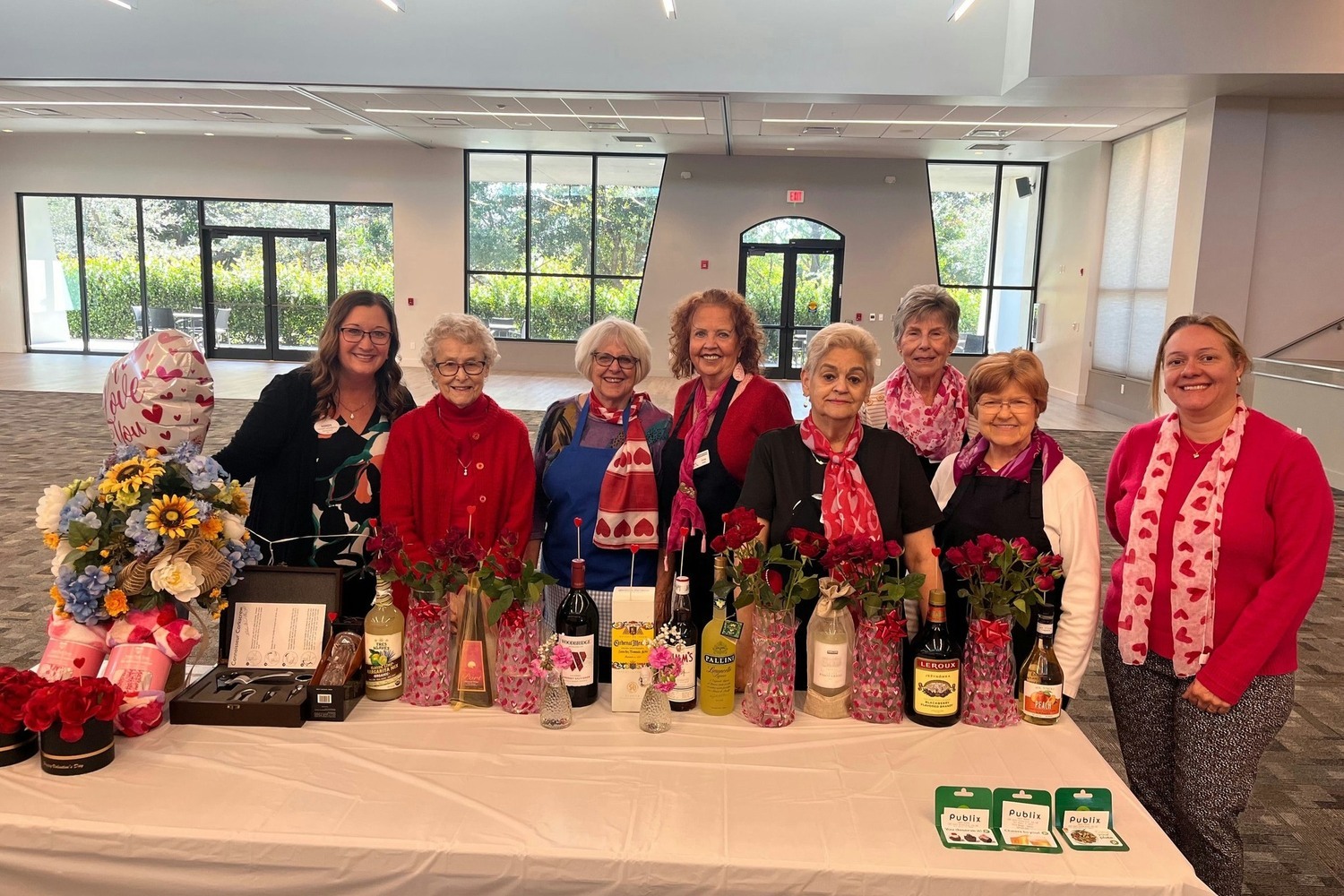 A cheerful group of residents poses together indoors, surrounded by colorful floral arrangements and festive decorations, celebrating community life at Barrington Terrace in Fort Myers, FL.