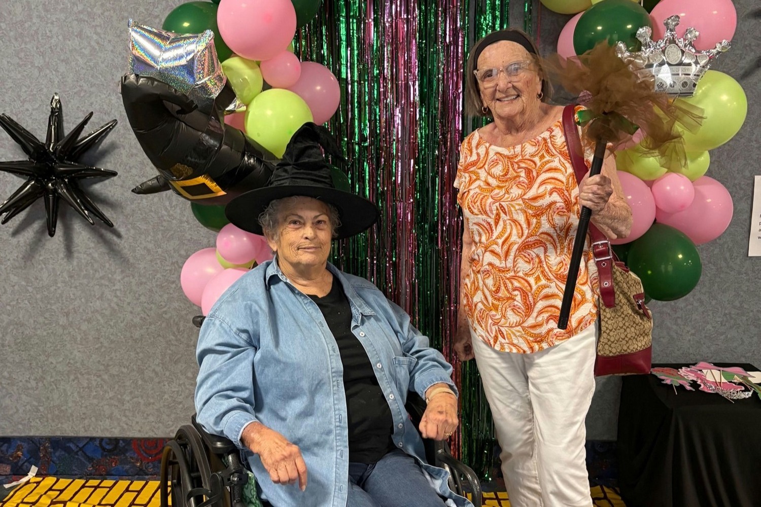 Residents enjoying a festive Halloween celebration at Barrington Terrace, a senior living community in Fort Myers, FL, dressed in costumes and posing in front of colorful balloon decorations and a shimmering green backdrop.