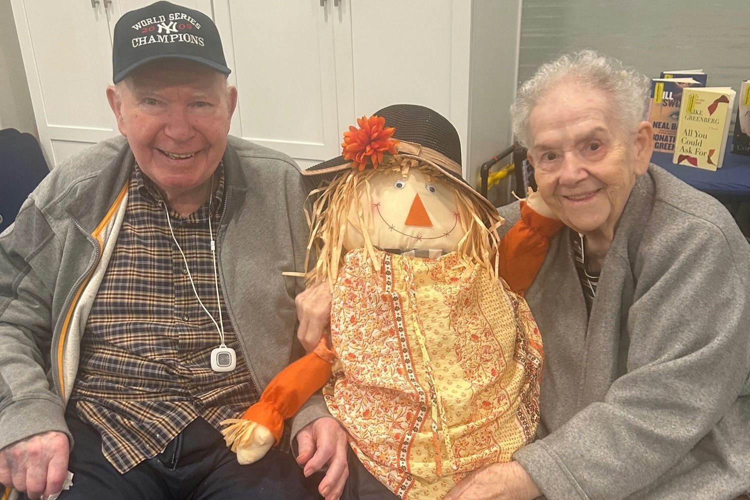 Two residents smiling and posing with a cheerful handmade scarecrow decoration at Barrington Terrace, an assisted living community in Fort Myers, FL, celebrating the fall season together.