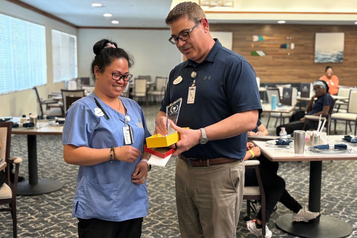 A staff member in scrubs smiles as she receives a crystal award from a colleague at Barrington Terrace, an assisted living community in Fort Myers, FL, celebrating the dedicated team who serve residents each day.