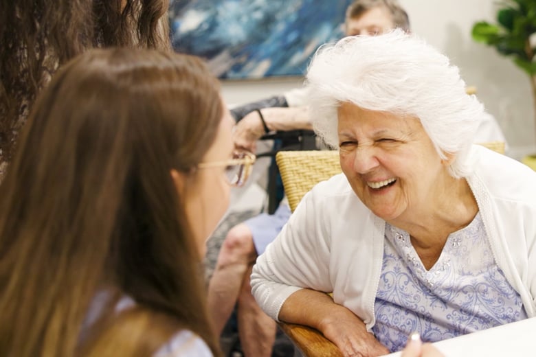 Two women share a joyful laugh together in a cozy indoor setting, reflecting the warm friendships and vibrant senior living lifestyle found throughout this senior living community.