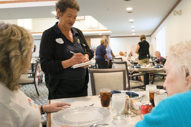 A staff member addresses residents gathered in the dining room at Barrington Terrace assisted living in Fort Myers, FL.