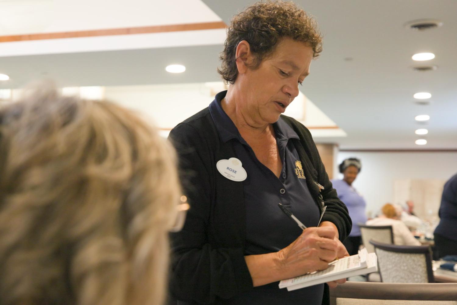 A staff member takes notes during an event in a bright common area at Barrington Terrace senior living in Fort Myers, FL.