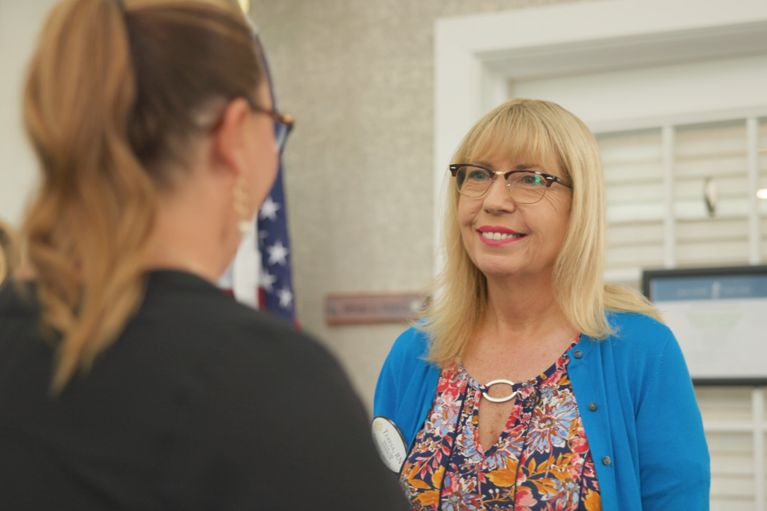 A staff member smiles brightly while speaking with someone in a welcoming common space at Barrington Terrace senior living in Fort Myers, FL.