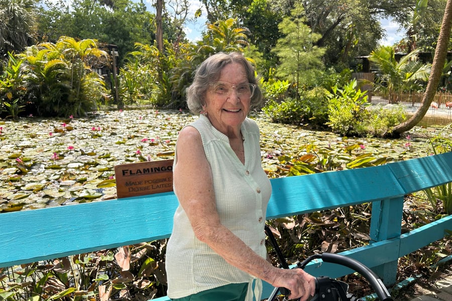 A resident smiles while seated on a teal bench beside a peaceful lily pond during an outing from this senior living community in Fort Myers, FL.