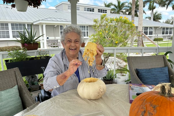 A resident laughs joyfully while carving a pumpkin outdoors at Barrington Terrace memory care in Fort Myers, FL.