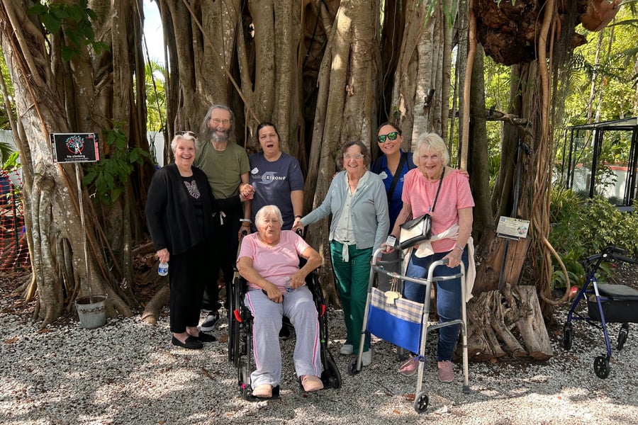 A cheerful group of residents and staff pose together beneath a large banyan tree during a community outing from Barrington Terrace senior living in Fort Myers, FL.