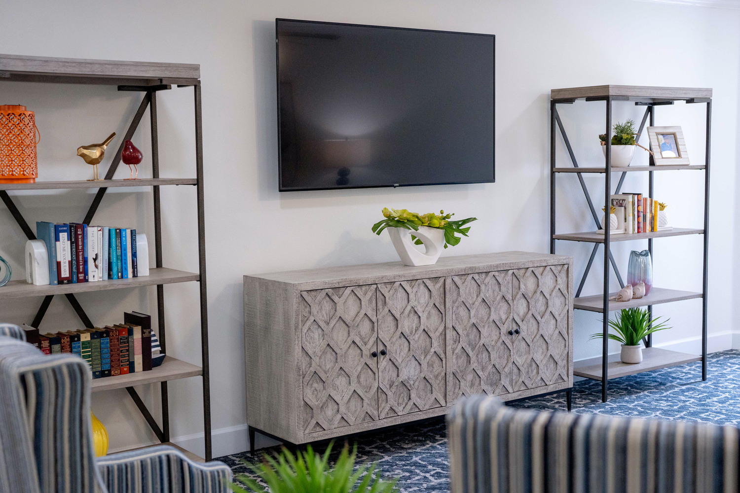 Bright apartment sitting area with a flat-screen TV, open shelving, and coastal-inspired decor at Barrington Terrace assisted living in Fort Myers, FL.