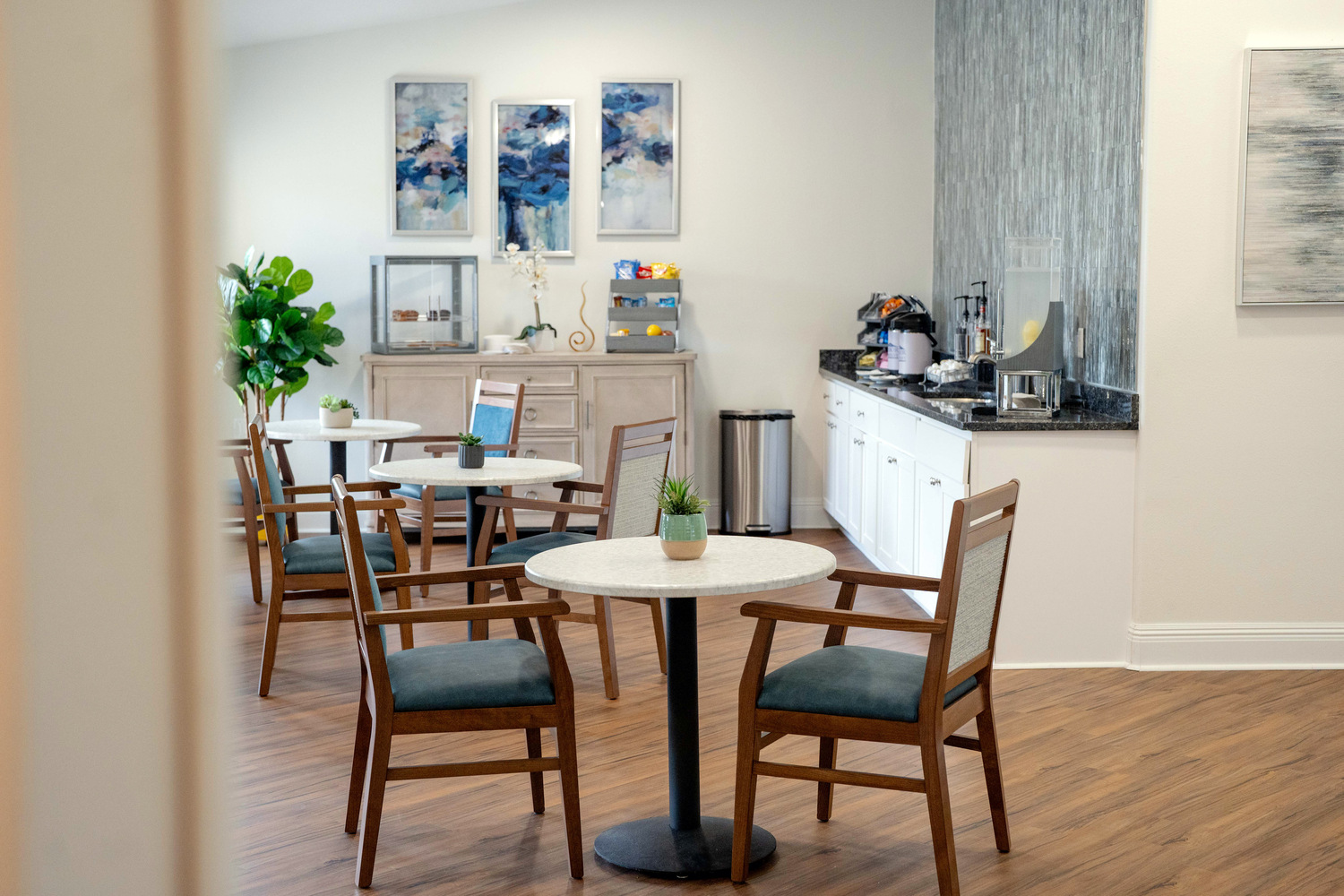 Bright coffee bar area with a round table, dark chairs, and decorative framed artwork at this assisted living community in Fort Myers, FL.
