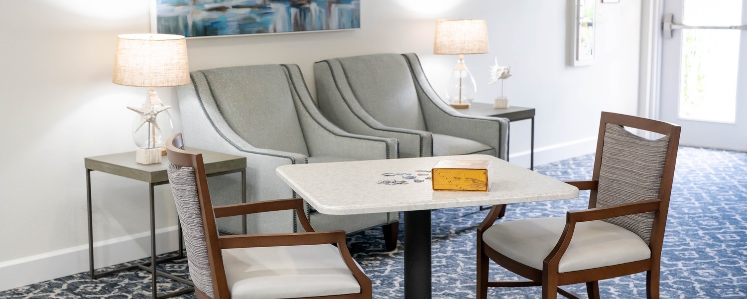 Comfortable sitting area featuring a large ocean-inspired painting, armchairs, and a flat-screen TV at this senior living community in Fort Myers, FL.