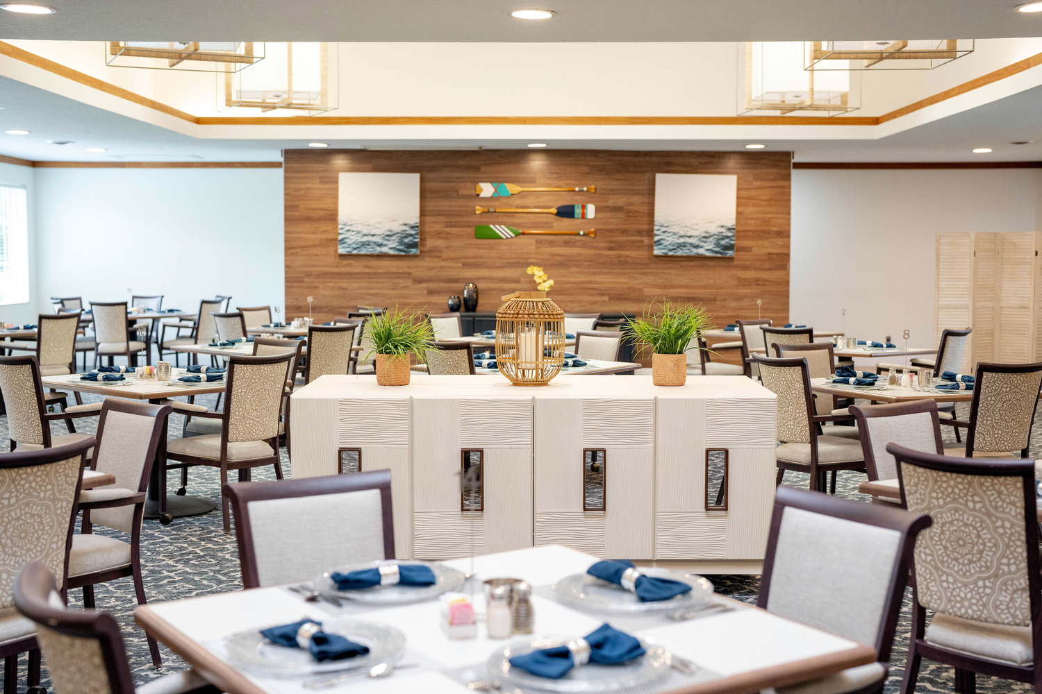 Elegantly set dining room with white tablecloths, wood-paneled walls, and warm overhead lighting at this senior living community in Fort Myers, FL.