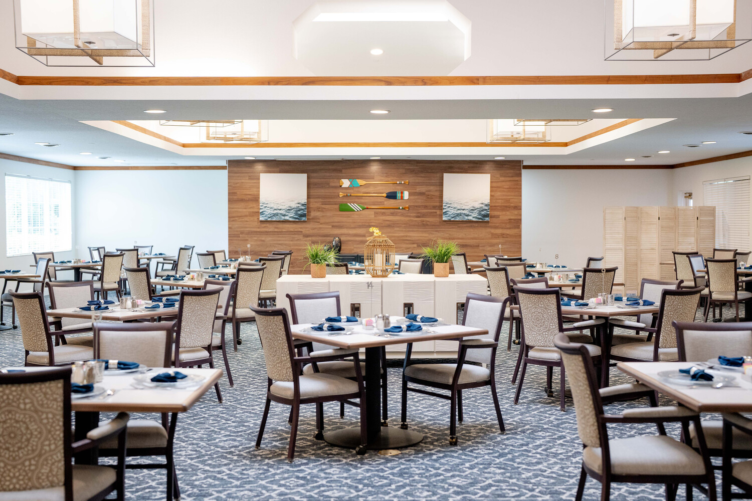 Spacious dining room with brick accent walls, neatly arranged tables, and blue place settings at Barrington Terrace assisted living in Fort Myers, FL.