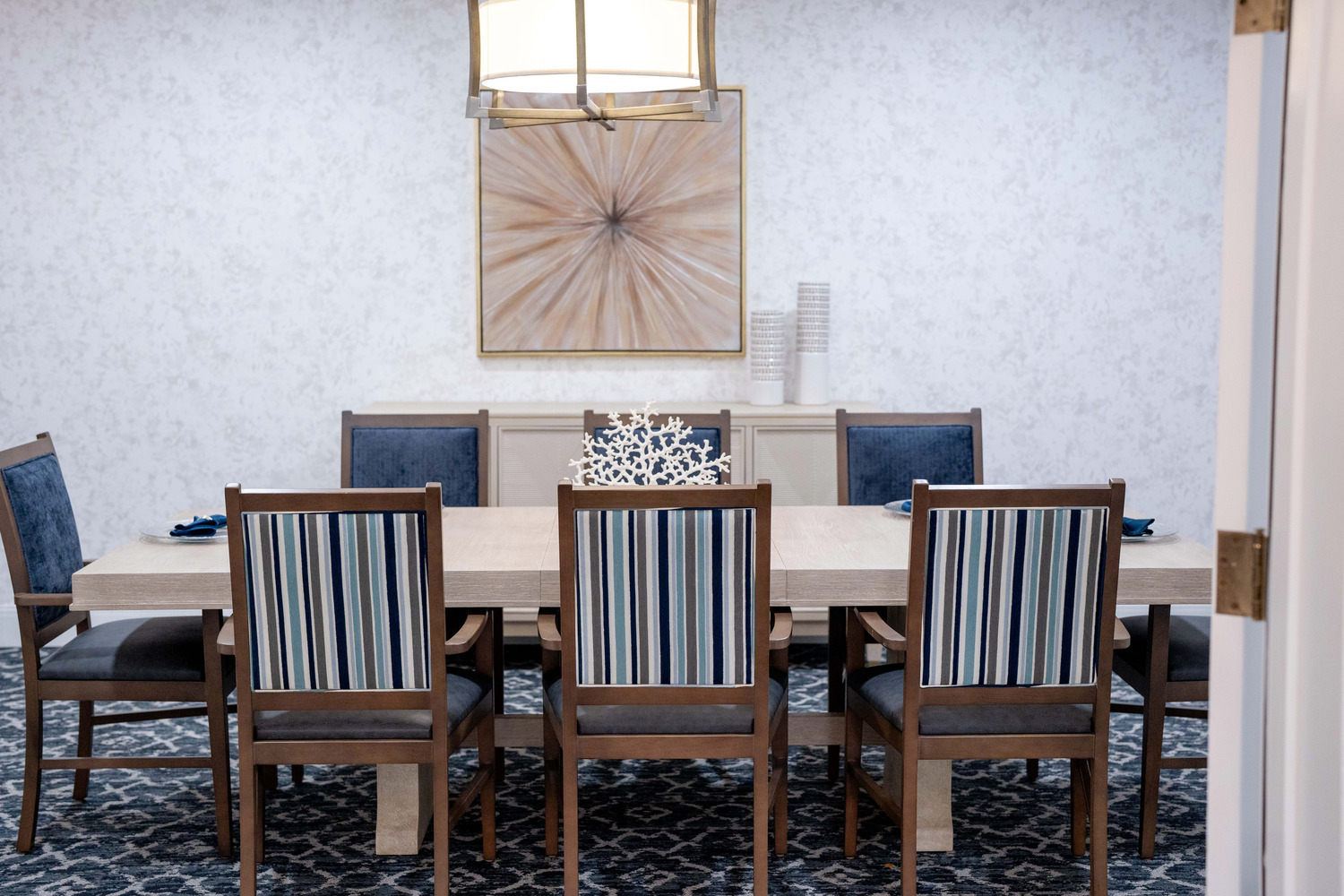Elegant private dining space with blue and white striped chairs and a decorative sunburst wall accent at this senior living community in Fort Myers, FL.