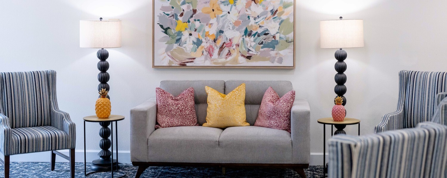 Elegantly furnished apartment living room with striped armchairs, a gray sofa with colorful accent pillows, and a vibrant abstract artwork at this senior living community in Fort Myers, FL.