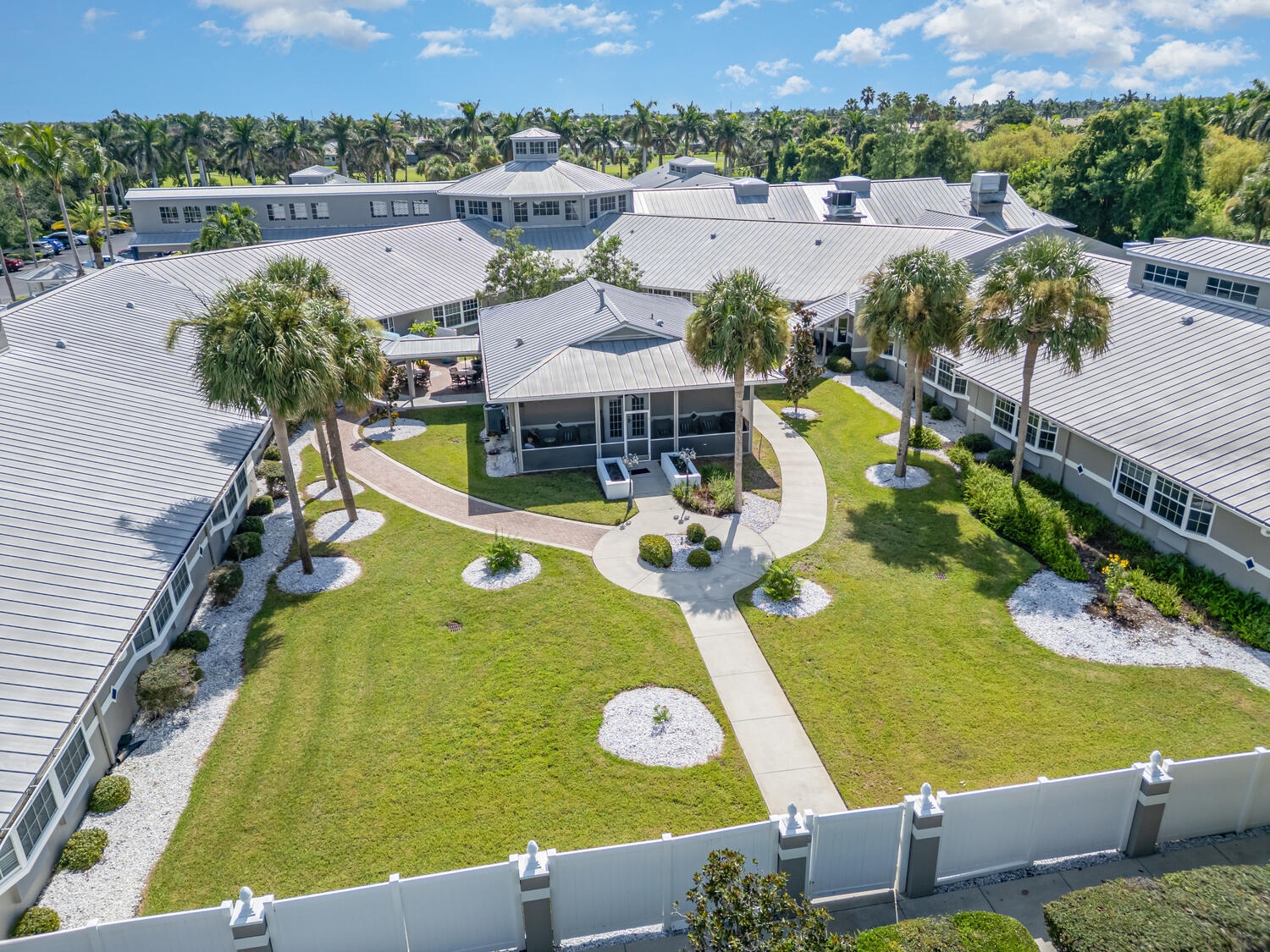 Overhead view of the resort-style senior living campus in Fort Myers, FL, with tropical palms, green lawns, and connected buildings.