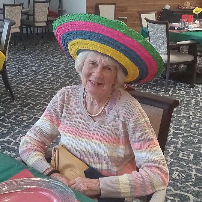 A resident grins while wearing a colorful oversized sombrero during a fun themed event at a senior living community near Cape Coral, FL.