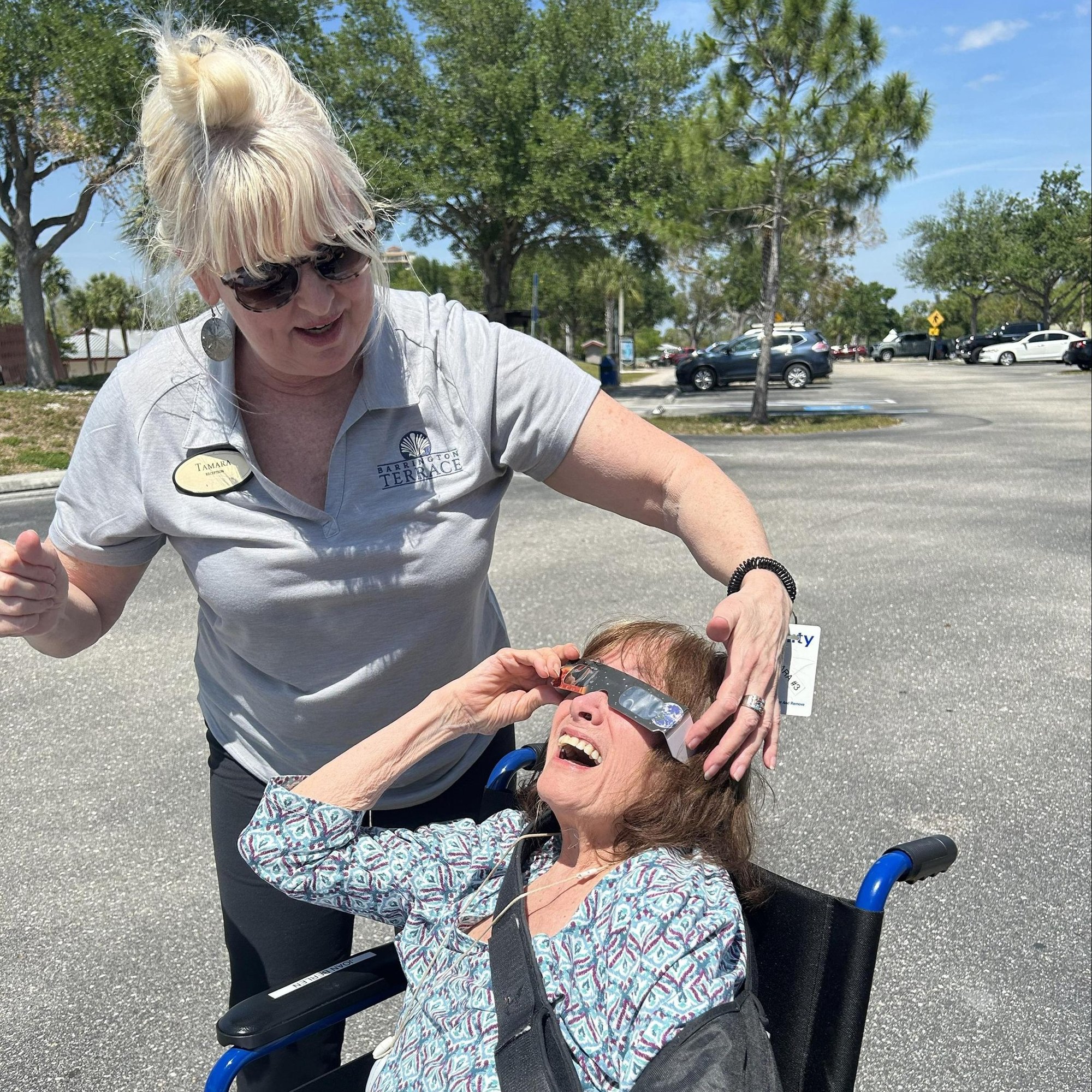 A staff member helps a resident look up at the sky outdoors on a sunny day at Barrington Terrace senior living in Fort Myers, FL.