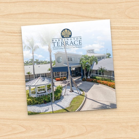 Square photo of Barrington Terrace Fort Myers building exterior with palm trees, gazebo, and circular driveway, displayed on a printed card against a wood-grain background.