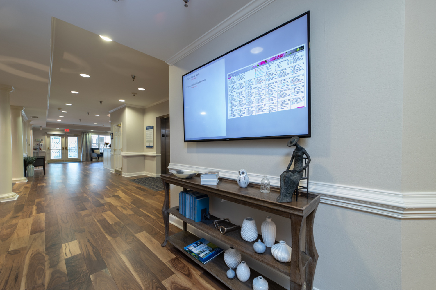 A bright hallway showcases rich wood flooring, a console table with curated decor, and a wall-mounted display, reflecting the polished, boutique senior living Greenville offers within this assisted living Greenville SC community.