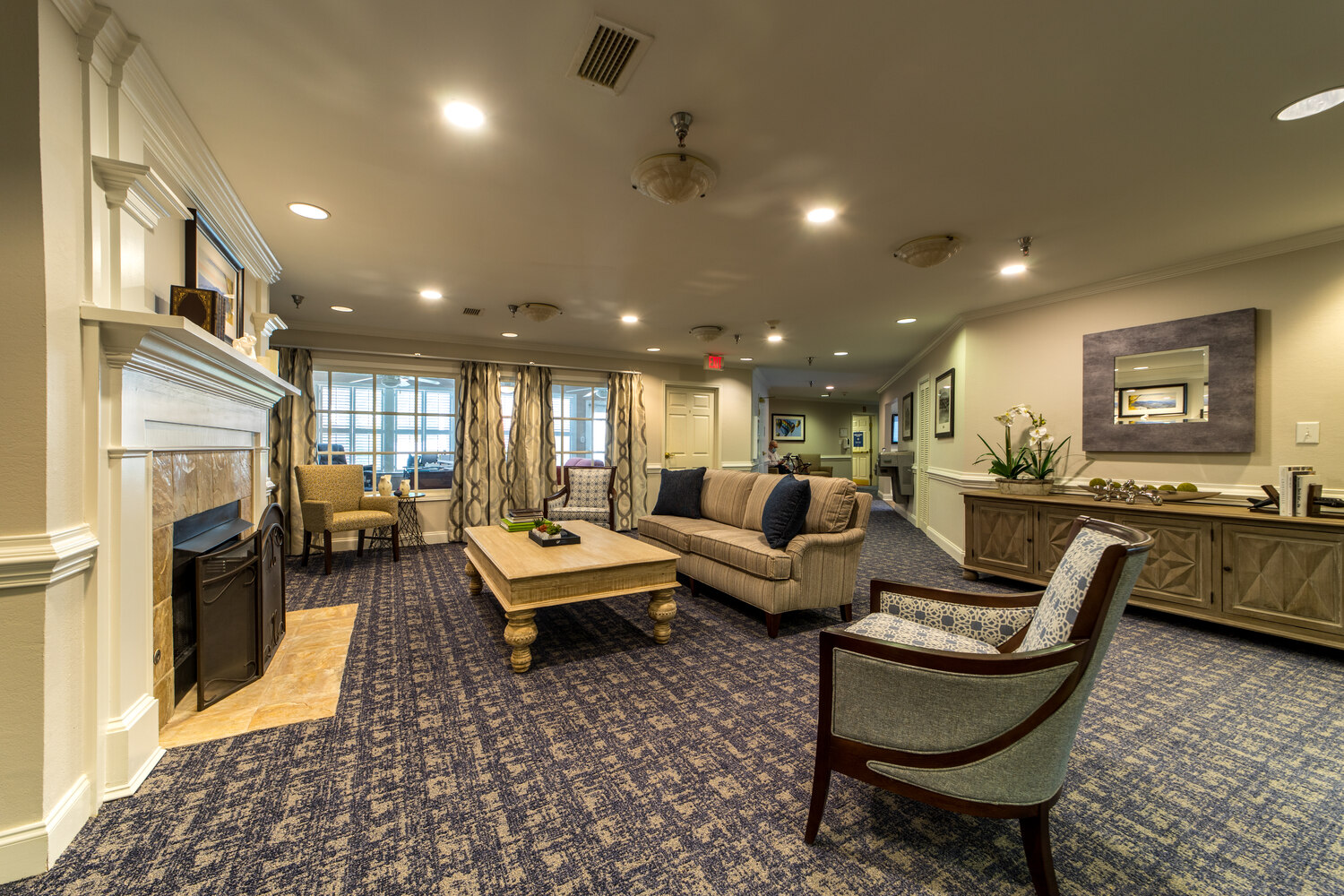 A cozy living room showcases a stone fireplace, plush seating, and a patterned area rug, capturing the resort-style assisted living Greenville area residents enjoy within this senior living Greenville SC community.