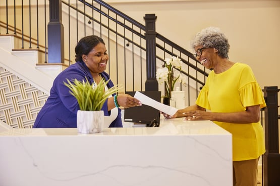 Staff member assisting resident at white front desk with stairs in the background
