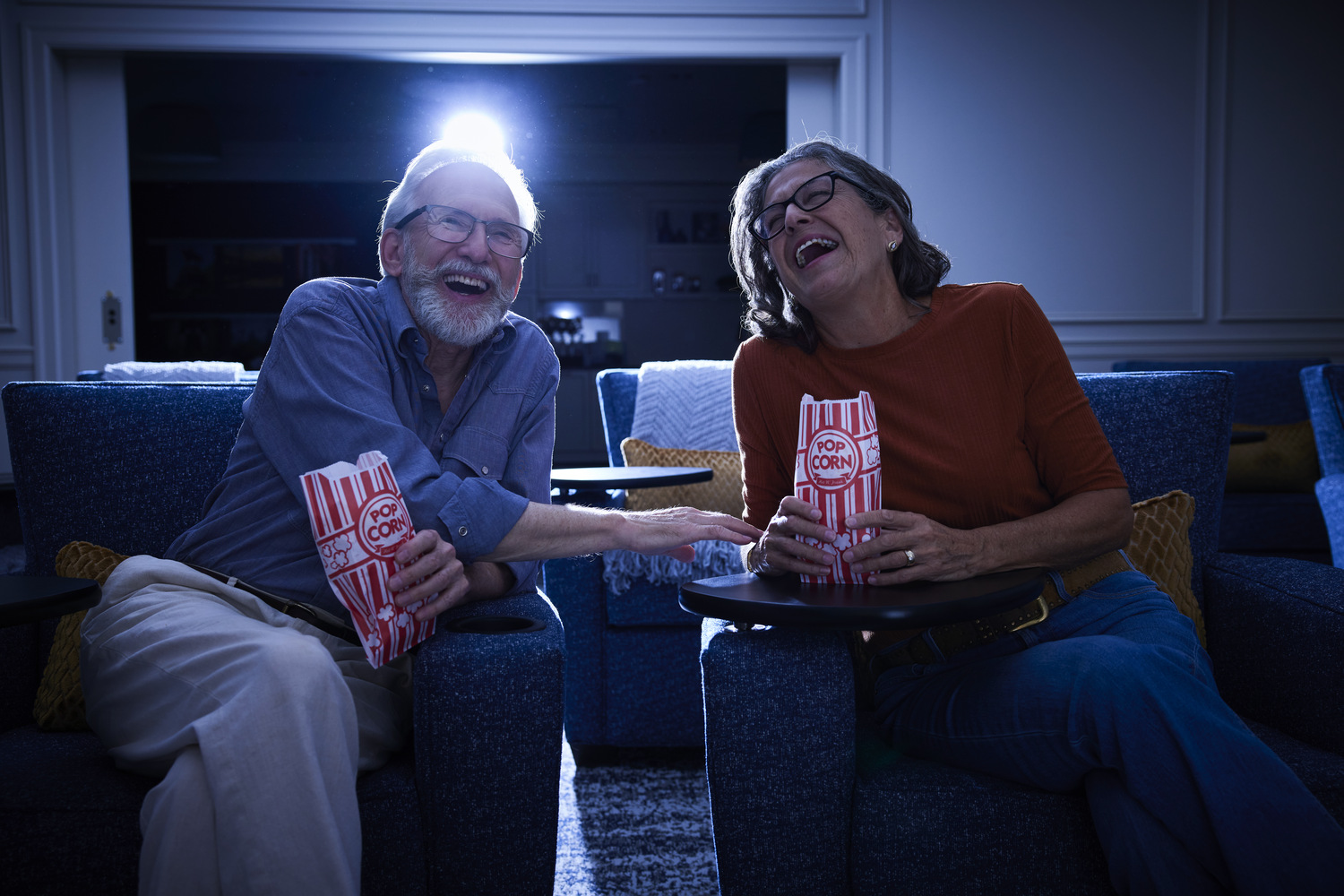 Two residents laugh together while enjoying popcorn at the on-site movie theater at Arbor Terrace, a senior living community in Lanham, MD, near Greenbelt, MD.