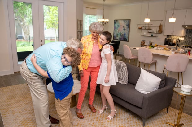 Grandparents hugging grandchildren with a grey couch and bar stools in the background