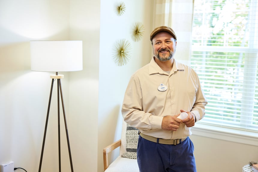 A friendly maintenance staff member smiles inside a resident's well-lit apartment at Arbor Terrace Senior Living, ensuring a worry-free lifestyle for seniors in Lanham, MD, near Greenbelt, MD.