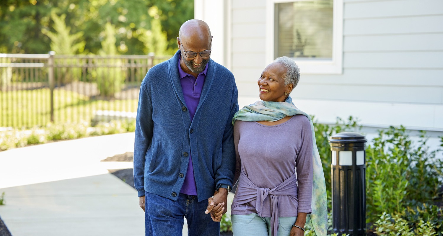 A couple strolls hand in hand along a peaceful outdoor path, reflecting the vibrant senior living lifestyle and everyday joy found throughout this senior living community.
